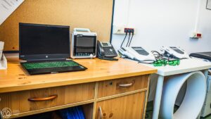 Laptop oraz sprzęt do fizykoterapii eżące na biurku i stole.